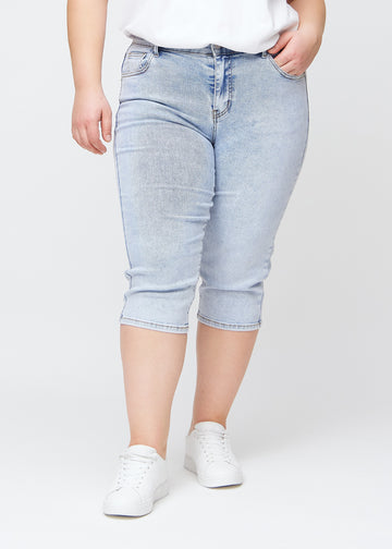 Lyseblå denim slim capris, farve Waves, med tætsiddende pasform og længde lige under knæet – set forfra på plus-size model.