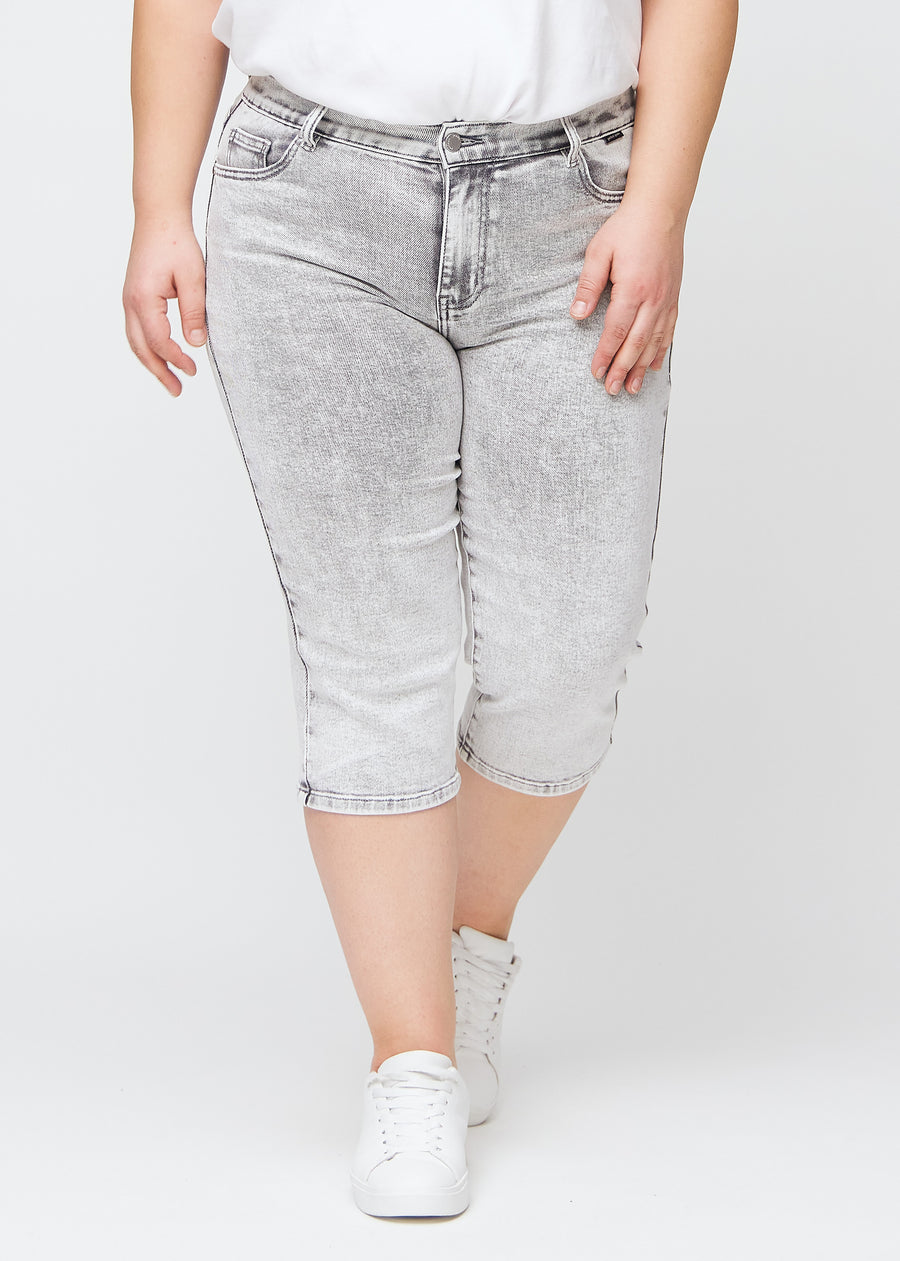 Lysegrå denim regular capris, modelnavn Ashes, som sidder lige til benet og slutter lige under knæet på en plus-size model, set forfra.