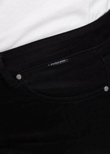 Nærbillede af sort jeansmateriale med Perfect Jeans logoetiket ved forlommekanten, på en plus-size model.