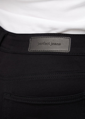 Nærbillede af sort jeansmateriale med Perfect Jeans læderpatch bagpå i taljen, på en plus-size model.