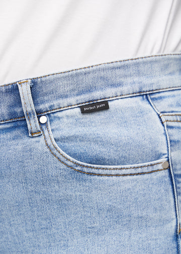 Close-up of light blue denim with Perfect Jeans logo label at the front pocket edge, on a plus-size model.