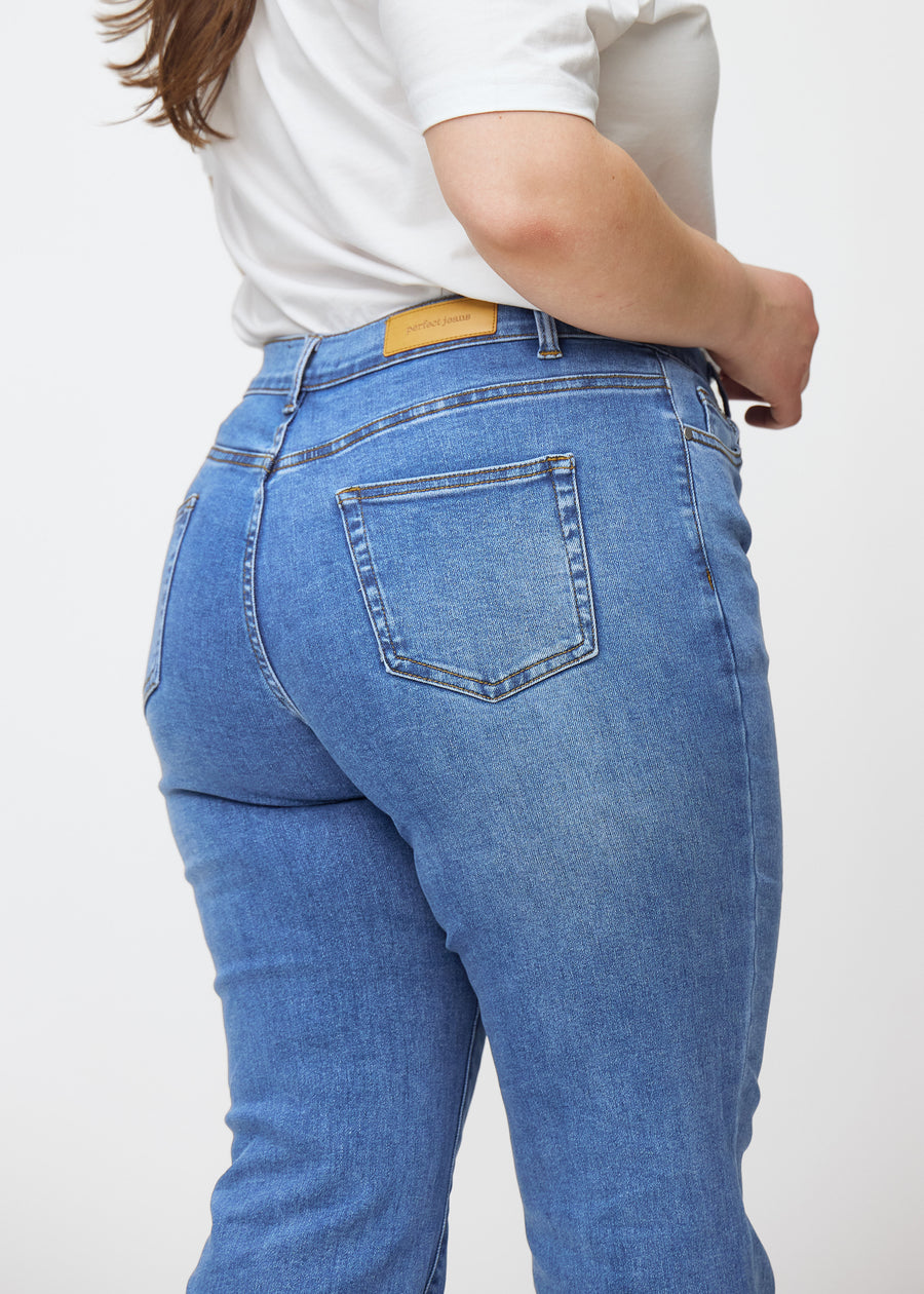 Blue mid-rise bootcut jeans in Rivers. Close-up back view on a plus-size model, showing the details.