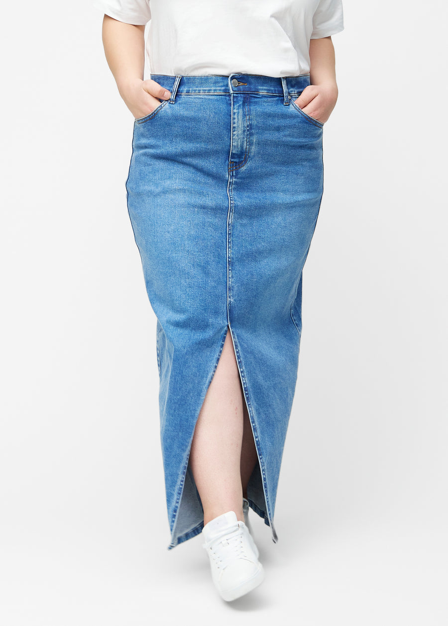 Lang, klassisk blå denimnederdel i farven Rivers med regulær pasform set forfra på plus-size model, med slids foran der starter lige under knæet.
