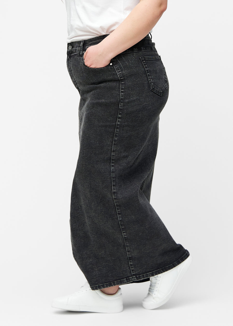 Lang, mørkegrå denimnederdel i farven Shadows med regulær pasform set fra siden på plus-size model, med synligt slids foran.