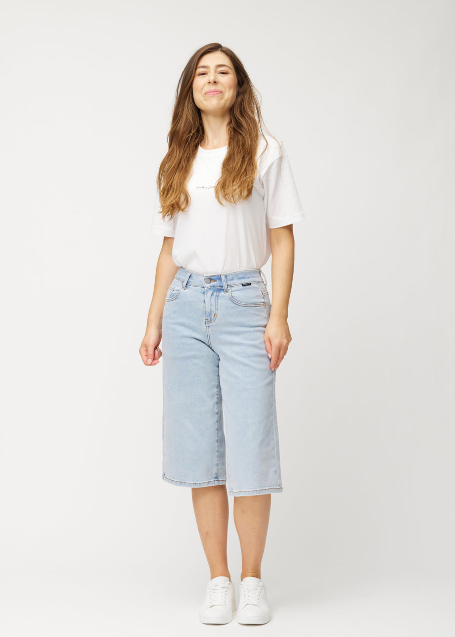 Full-length view of a model wearing loose, light blue Waves denim capris that end just below the knee.