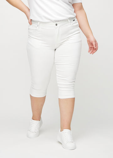 White skinny capris, model name Marguerites, which fit closely to the leg and end just below the knee on a plus-size model, seen from the front.