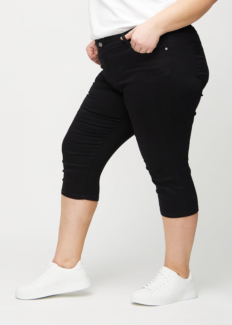 Black skinny capris seen from the side on a plus-size model.