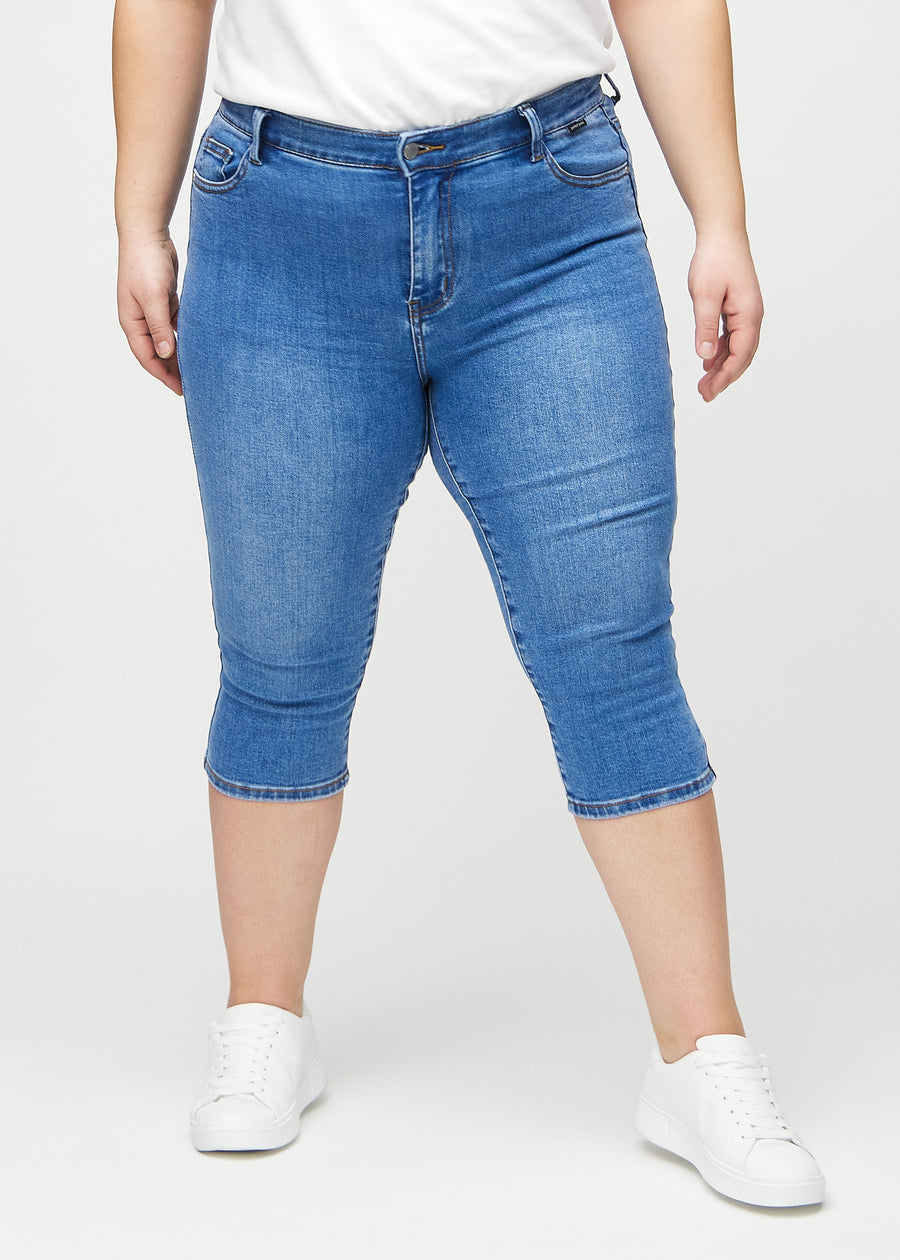 Denim skinny capris, model name Rivers, which fit closely to the leg and end just below the knee on a plus-size model, seen from the front.