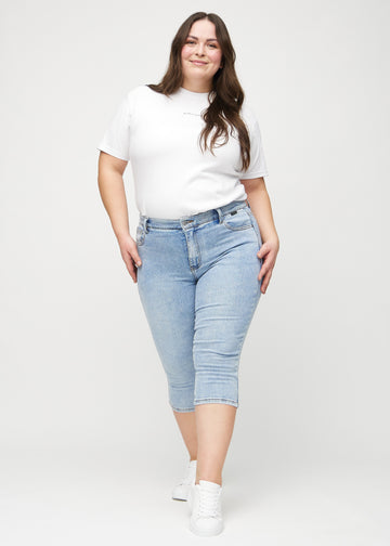 Skinny capris for women in light blue denim, color Waves. Full-length view of a plus-size model wearing the capris.
