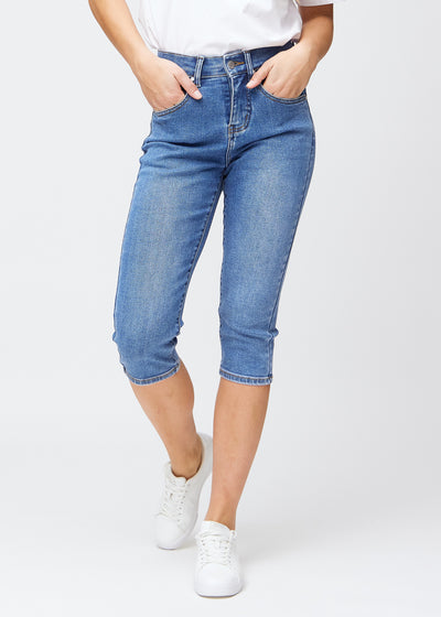 Slim capris for women in blue denim, color Rivers. Front view on a model, showing the fitted cut ending just below the knee.
