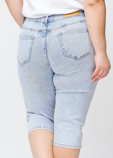 Close-up image of the back on a plus-size model wearing light blue denim slim capris, with focus on pockets and stitching details.