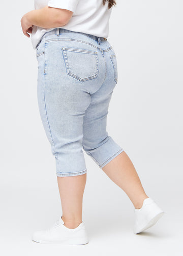 Light blue denim slim capris in the colour Waves, seen from the side on a plus-size model, so you can see the fit and silhouette.