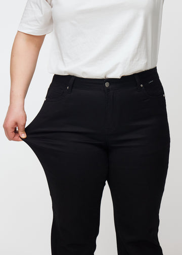 Black mid-rise bootcut jeans in Ravens. A plus-size model stretches the jeans at the thigh to show the fabric&