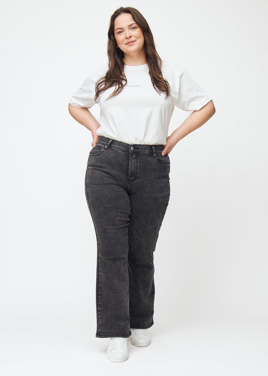Dark grey mid-rise bootcut jeans in Shadows. Full-length view of a plus-size model wearing the jeans.