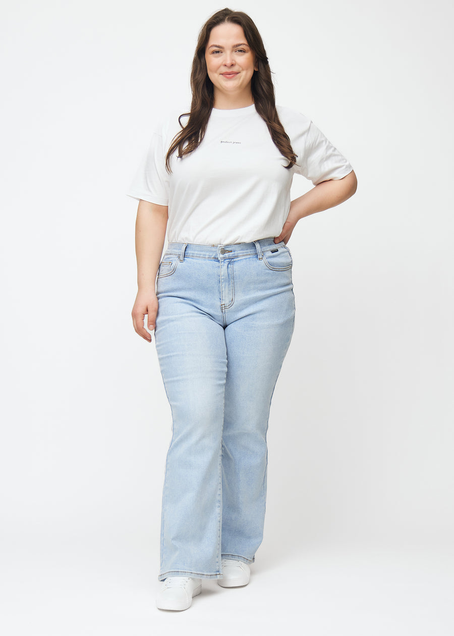 Light blue mid-rise bootcut jeans in Waves. Full-length view of a plus-size model wearing the jeans.
