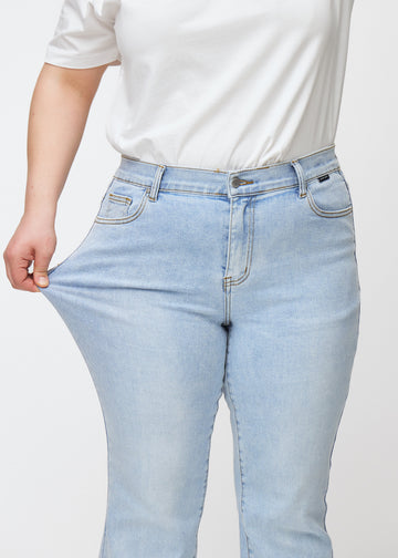 Light blue mid-rise bootcut jeans in Waves. A plus-size model stretches the jeans at the thigh to show the fabric&