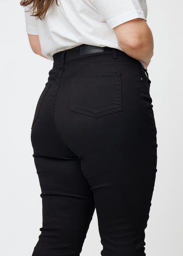 The image shows a close-up of black plus size high rise jeans for women in the color Ravens in skinny fit, seen from the back.