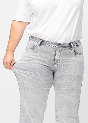 The plus-size model stretches the jeans at the thigh to show the stretch.