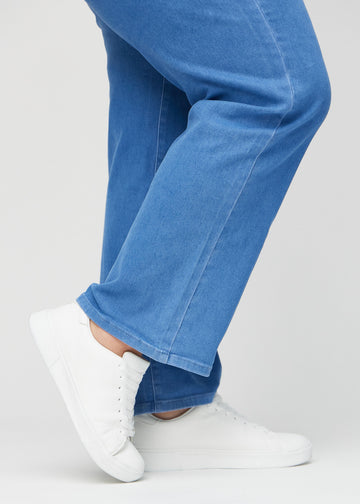 Loose jeans for women in blue, color Geraniums. Close-up at the ankles on a plus-size model, showing the wide leg openings.