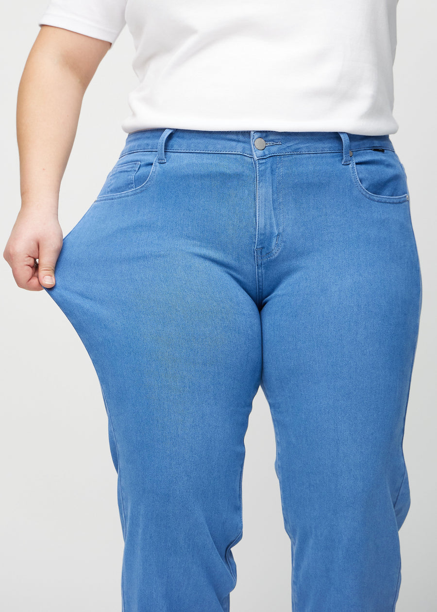 Loose jeans for women in blue, color Geraniums. A plus-size model stretches the denim at the thigh to show the fabric&