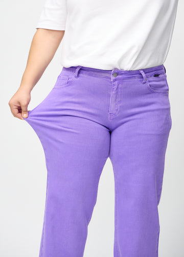 A plus-size model stretches the jeans at the thigh to show the stretch.
