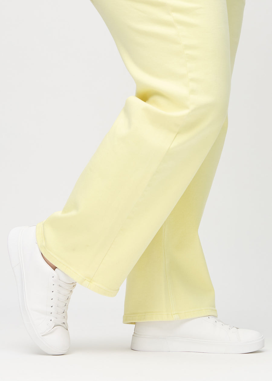 Loose jeans for women in light yellow, color Lemonades. Close-up at the ankles on a plus-size model, showing the wide leg openings.