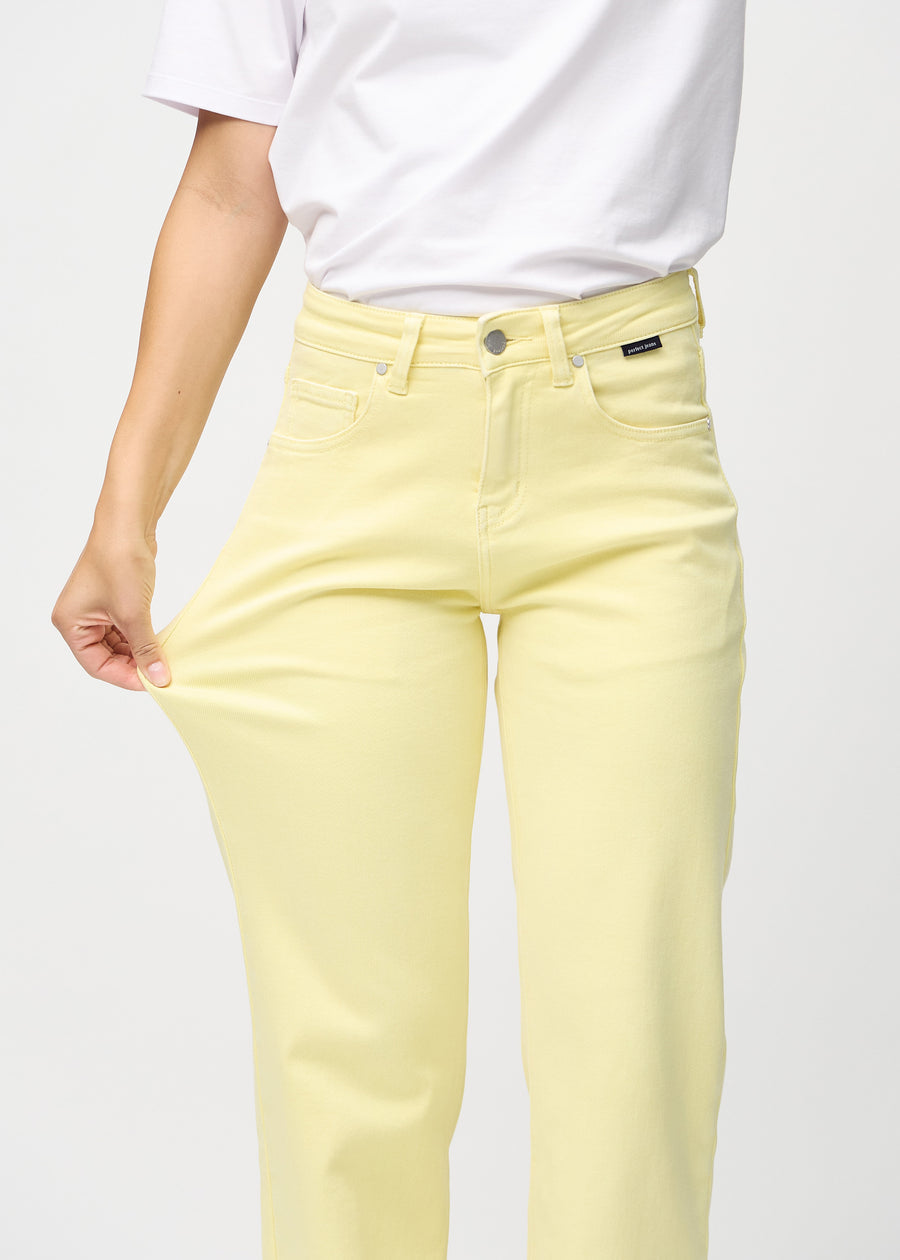 Loose jeans for women in light yellow, color Lemonades. A model stretches the denim at the thigh to show the fabric&