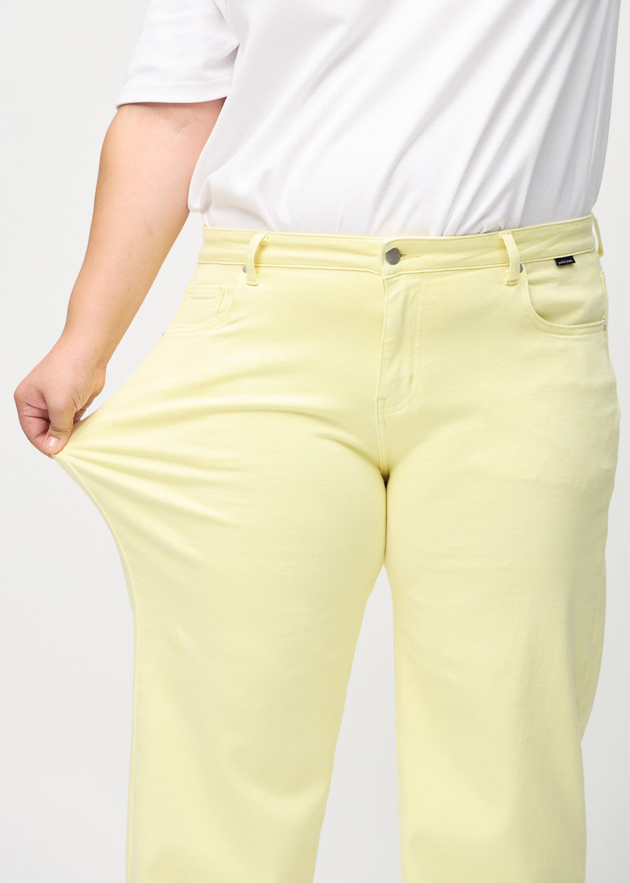 Loose jeans for women in light yellow, color Lemonades. A plus-size model stretches the denim at the thigh to show the fabric&