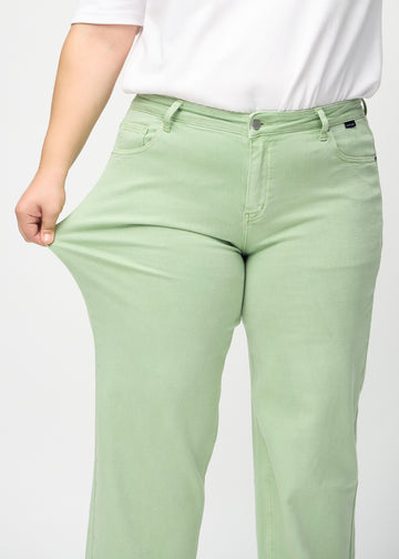Loose jeans for women in light green, color Mints. A plus-size model stretches the denim at the thigh to show the fabric&