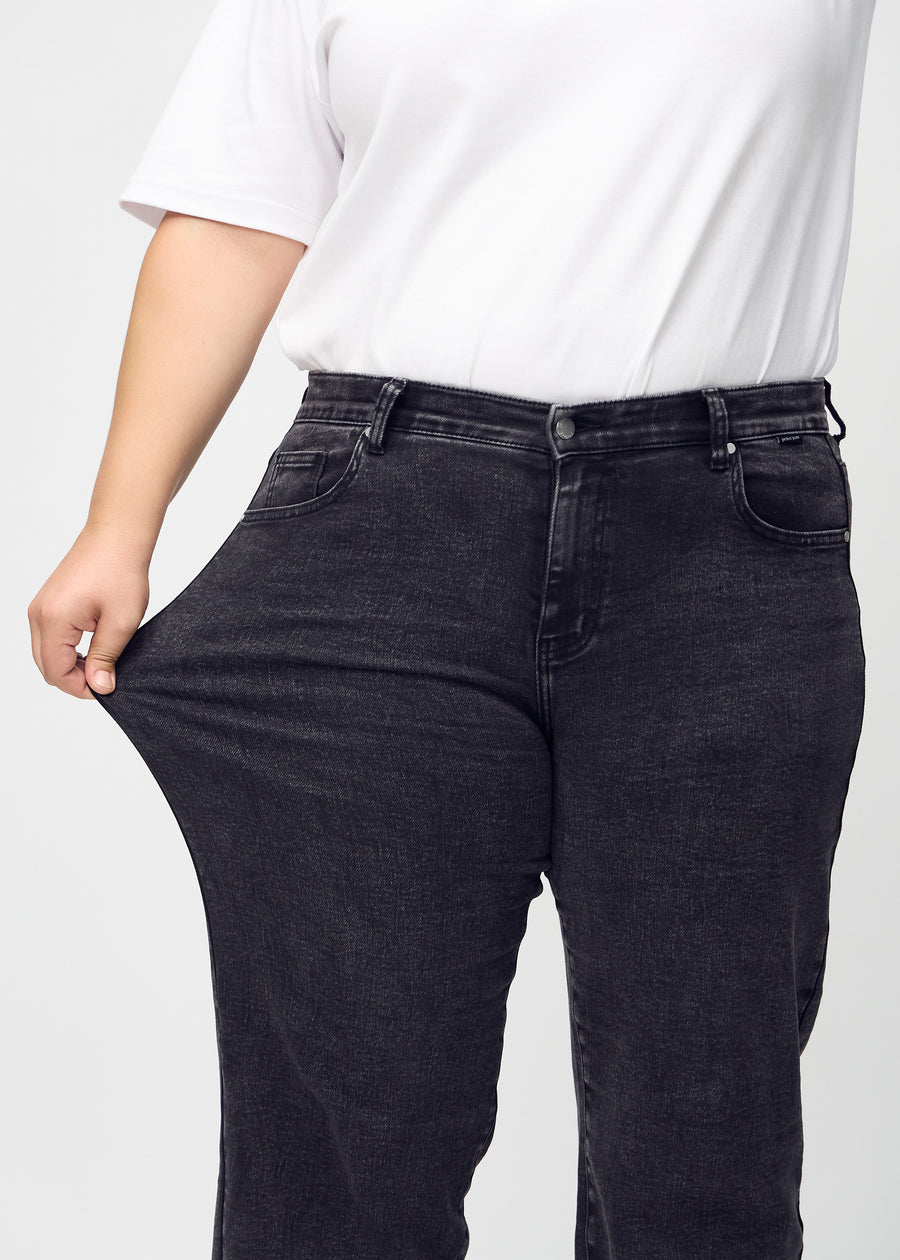The plus-size model stretches the jeans at the thigh to show the stretch.