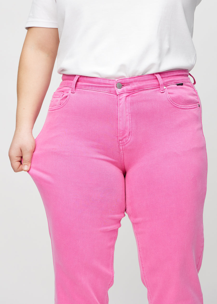 Regular jeans for women in light pink, color Flamingos. A plus-size model stretches the fabric at the thigh to show its stretch.