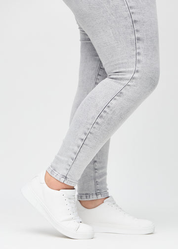 Skinny jeans for women in light grey, color Ashes. Close-up of the snug-fitting leg openings at the ankles on a plus-size model.