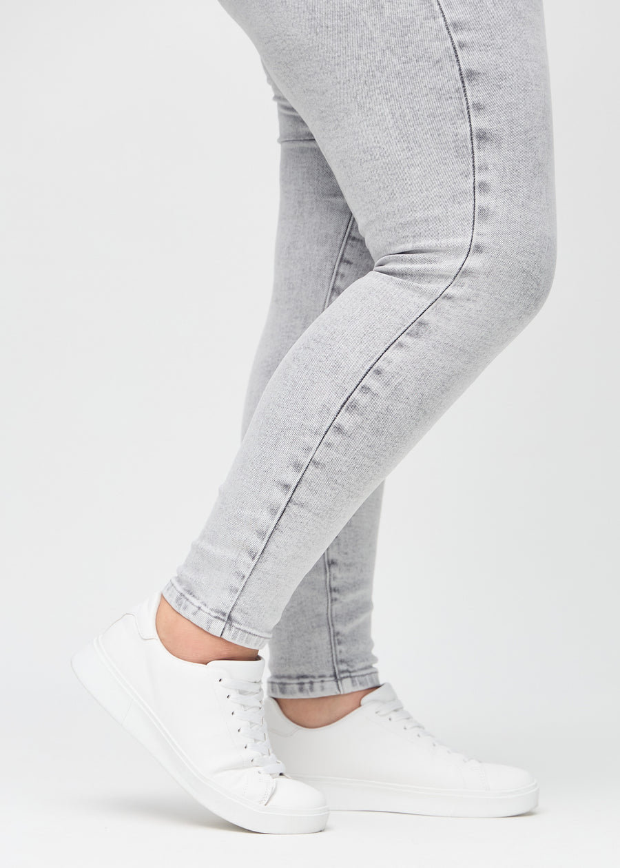 Skinny jeans for women in light grey, color Ashes. Close-up of the snug-fitting leg openings at the ankles on a plus-size model.