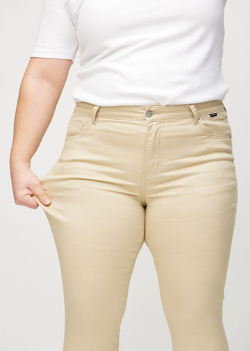 The plus-size model stretches the jeans at the thigh to show the stretch.