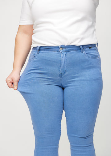 Skinny jeans for women in blue, color Geraniums. A plus-size model stretches the jeans at the thigh to show the fabric&