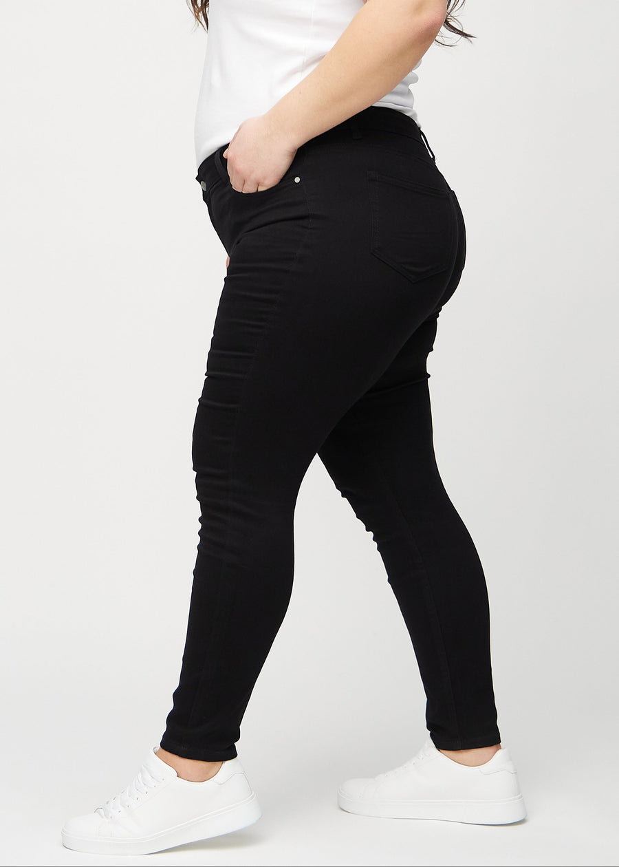Black skinny jeans seen from the side on a plus-size model.