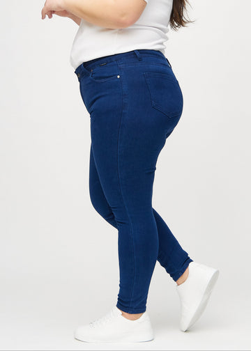 Dark blue skinny jeans viewed from the side on a plus-size model.