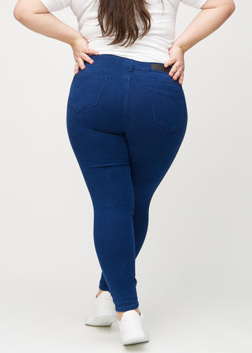 Dark blue skinny jeans viewed from the back on a plus-size model, so you can see the entire product.