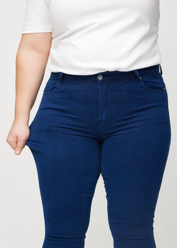 The plus-size model stretches the jeans at the thigh to show the stretch.