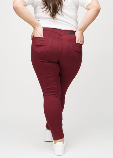 Dark red skinny jeans seen from the back on a plus-size model, so the entire product can be seen. 