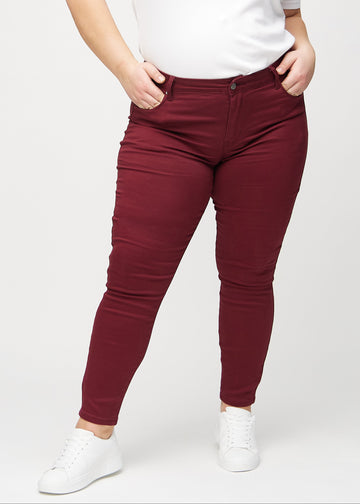 Dark red skinny jeans, model name Santas, which fit closely to the leg on a plus-size model, seen from the front.
