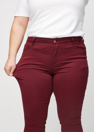 The plus-size model stretches the jeans at the thigh to show the stretch.