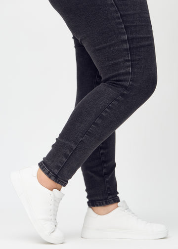 Skinny jeans for women in dark grey, color Shadows. Close-up of the snug-fitting leg openings at the ankles on a plus-size model.