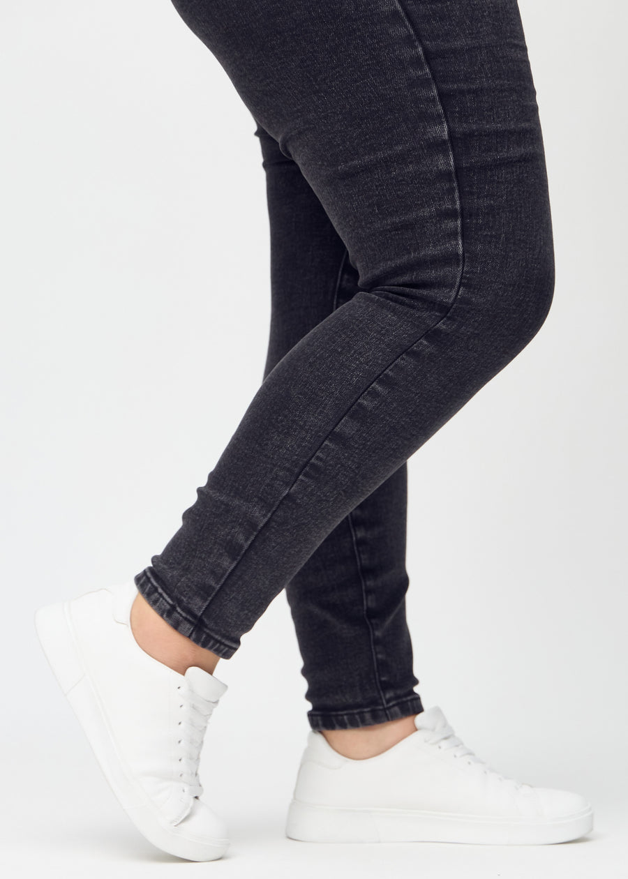 Skinny jeans for women in dark grey, color Shadows. Close-up of the snug-fitting leg openings at the ankles on a plus-size model.