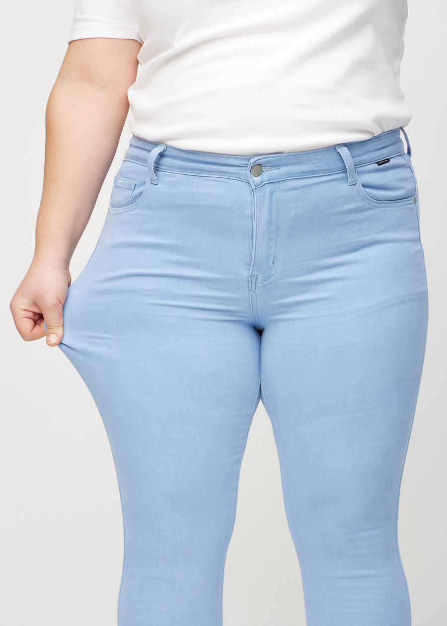 Skinny jeans for women in light blue, color Skies. A plus-size model stretches the jeans at the thigh to show the fabric&