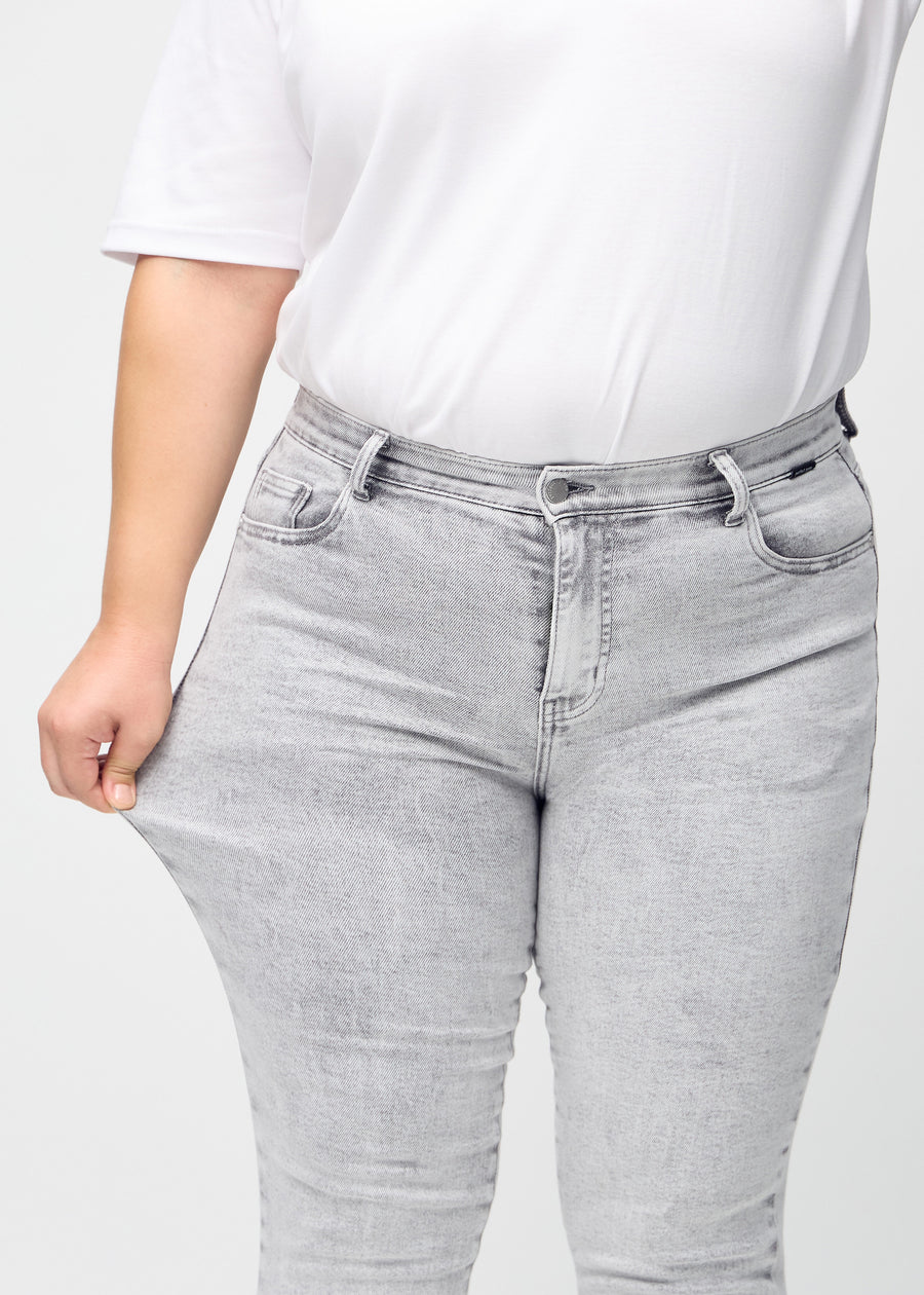 Slim jeans for women in light grey, color Ashes. A plus-size model stretches the jeans at the thigh to show the fabric&