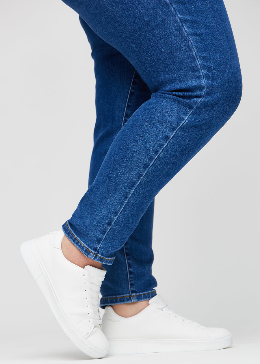 Slim jeans for women in dark blue, color Oceans. Close-up at the ankles on a plus-size model, showing the fit at the leg openings.