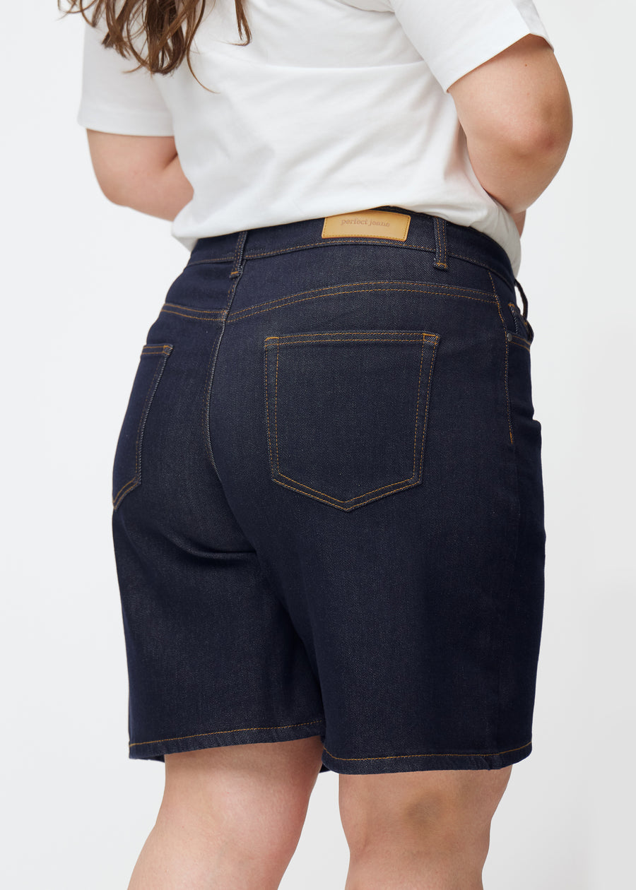 Deep dark blue denim shorts for women in the colour Midnights seen from the back in close-up on a plus-size model.