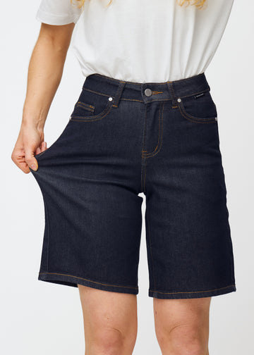 Model stretches deep dark blue denim shorts for women in the colour Midnights at the thigh to show the material’s stretch.