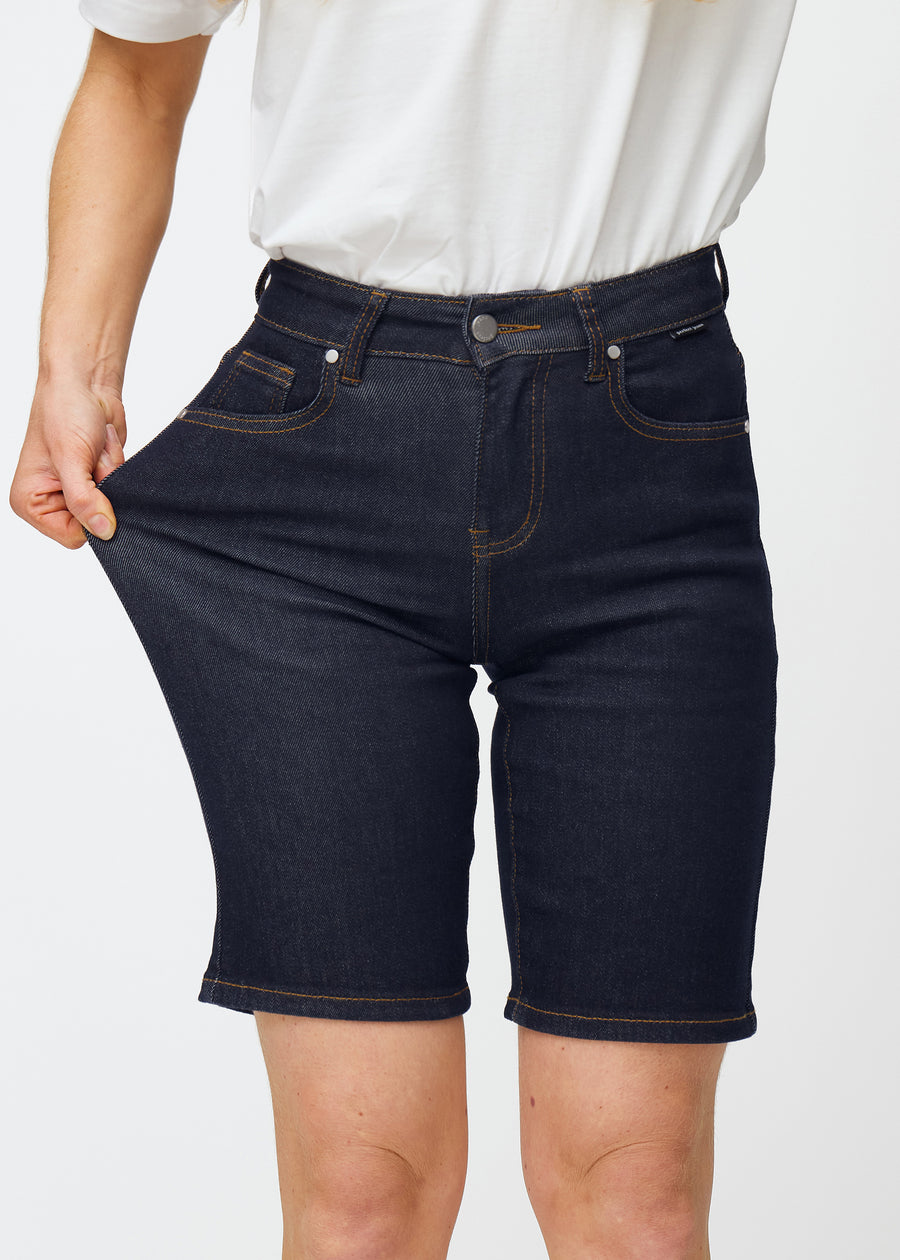 Model stretches deep dark blue denim shorts for women in the colour Midnights at the thigh to show the material’s stretch.